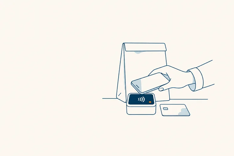 Une main tend un téléphone au-dessus d’un terminal de paiement posé sur un comptoir.